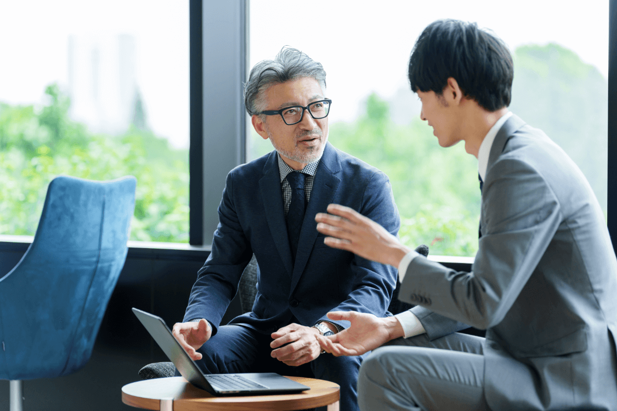 落ち着いた雰囲気の中年男性が若い男性と対話しているビジネスシーン